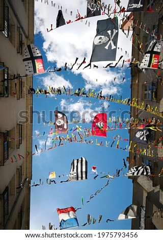 Different flags: those of France, of region of Brittany, of Nantes city, Black Jack and the Jolly Roger hung on the ropes stretched between buildings in the street of Nantes city in background of sky