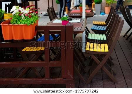 Colorful restaurant chairs in the garden are waiting for customers. The garden decorated with pots with daisies is eye-catching.                               