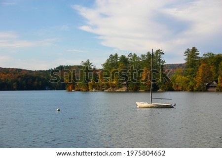 
Sailboat anchored in calm lake with cabins and fall color trees in background