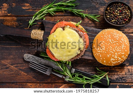 Beef burger with cheese, tomatoes, onions, cucumber and lettuce. Dark wooden background. Top view