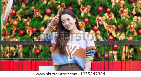 Asian beautiful girl wears colorful sweater and stands in front of Christmas tree in New Year celebrate theme.