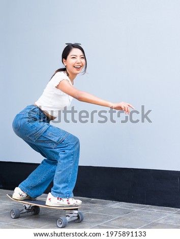 Asian cute girl or woman happy on surfing skateboard in front of cool wall with copy space on wall in daylight time, summer holiday.
