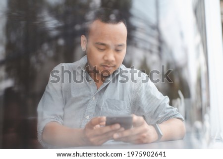 Happy Asian man using smartphone at cafe table.