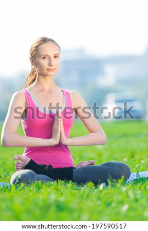 Beautiful sport woman doing stretching fitness exercise in city park at green grass. Yoga lotus pose