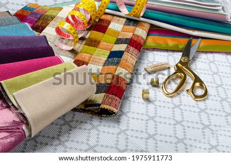 Closeup of catalogs of textile for furniture, scissors, thread,thimbles on the workplace