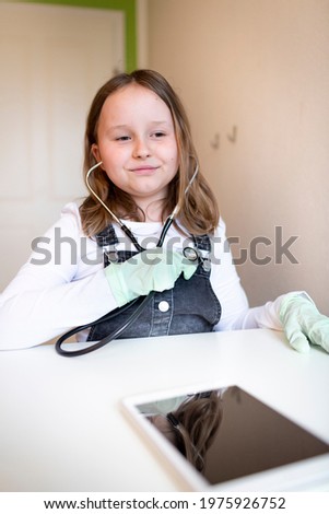 pretty young schoolgirl sitting on her desk in room at home playing with stethoscope during home schooling