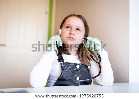 pretty young schoolgirl sitting on her desk in room at home playing with stethoscope during home schooling