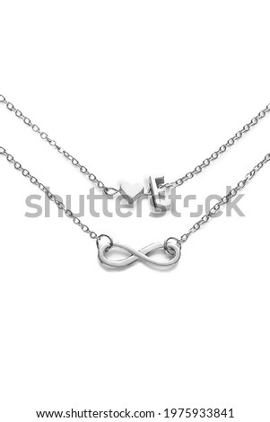 Cropped shot of two silver chains with charms shaped as infinity sign, heart and letter E. The piece of elegant jewelry is isolated on the white background. 