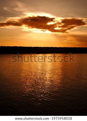 The sun is approaching the horizon. A cloud covers the sun. The lights of the sun are reflected in the sea. Everything is painted yellow. The horizon line is blocked by a breakwater.