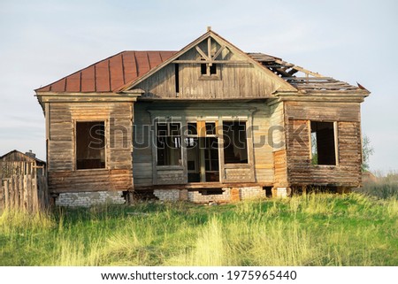 Poor wooden dilapidated house against the sky, surrounded by greenery. Royalty-Free Stock Photo #1975965440