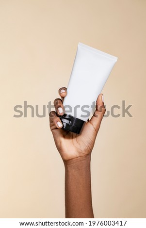 Black woman holding an unlabeled cream tube Royalty-Free Stock Photo #1976003417