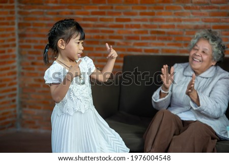 Happy Grandma with granddaughter,Little granddaughter dancing in living room enjoy priceless time together at funny weekend activities concept. Royalty-Free Stock Photo #1976004548