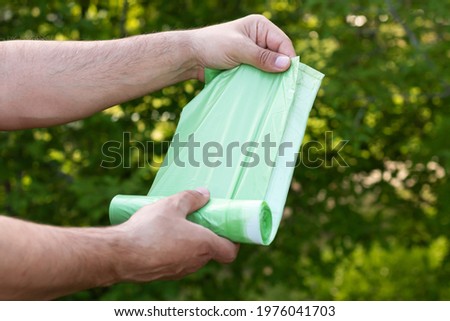 Man holding eco plastic garbage bio bag in roll outdoors, bag for composting organic trash Royalty-Free Stock Photo #1976041703