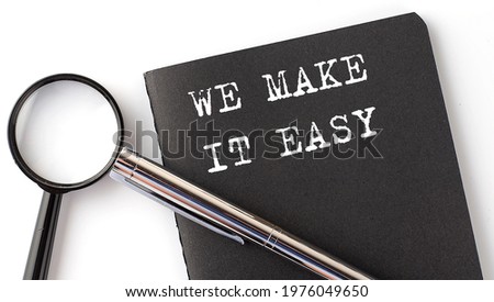 WE MAKE IT EASY - business concept, magnifier with white text message on the black notebook