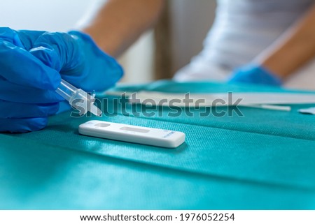 Female health care worker wearing blue surgical gloves and placing a sample in the covid-19 antigen diagnostic drug on a green surgical fabric 