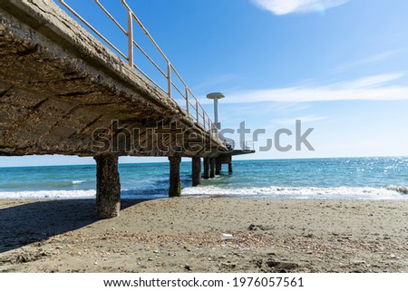 Concrete pier on the seafront of Ostia, black beach and calm sea with clear sky and some clouds on the horizon