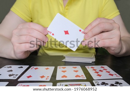 Close-up of hands holding ace of diamonds. The woman on the table is playing solitaire. Board and card games, home leisure activities. Card reading, cartomancy. Royalty-Free Stock Photo #1976068952
