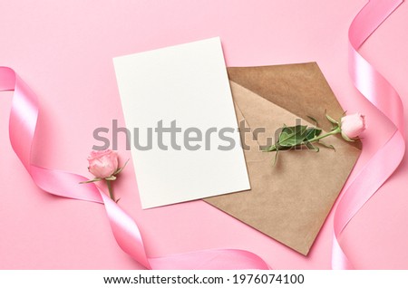 Greeting card with envelope, pink ribbon and rose flower, mockup with copy space on paper background, top view