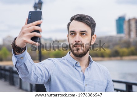 Portrait of a man businessman with a beard in a shirt who takes a selfie on a smartphone