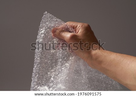 Male hand popping bubbles of bubble wrap on gray background.