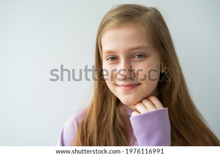 portrait of beautiful teenage girl with long hair in purple hoodie standing against white wall.