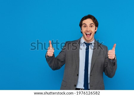 happy smiling man in suit showing thumbs up gesture on blue background