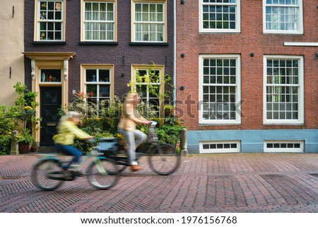 Motion blurred bicycle rider cyclist woman and child on bicycle very popular means of transport in Netherlands in street with old houses of Delft, Netherlands