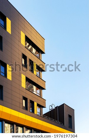Fragment of a new elite residential building or commercial complex against a blue sky. Part of urban real estate. Yellow-brown modern ventilated facade with windows.