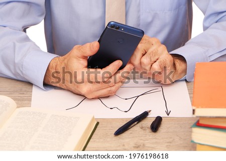 A businessman in a blue shirt and beige tie in the office holds a smartphone in his hand, a globe, books and glasses on the table. A student in the librar with a phone in his hands .