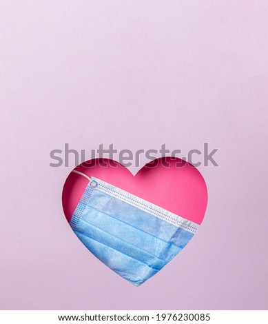 The medical blue mask is in a pink heart on a purple background. Minimal concept of love and medicine. Copy space.