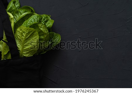close-up of a reusable black grocery bag with salad on a black background