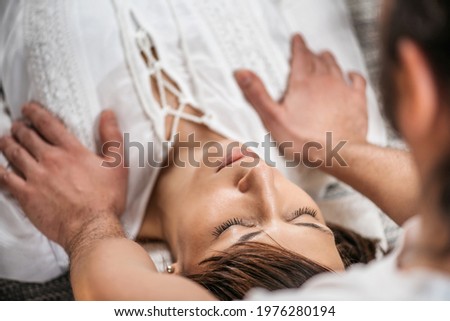 Thai Healing Massage - Energy work between Practitioner and Client. Traditional Thai massage therapist holding hands on the female patient's shoulder.   Royalty-Free Stock Photo #1976280194