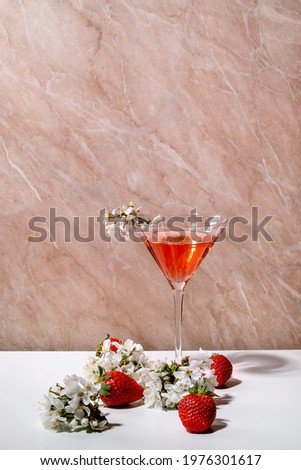 Concept of strawberry alcoholic or non-alcohol cocktail in martini glass decorated with blooming branches of cherry tree over white and pink texture background. Copy space