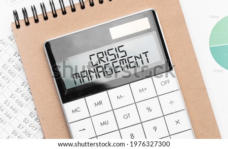 Calculator with text crisis management with craft colored notepad pen and financial documents. Royalty-Free Stock Photo #1976327300