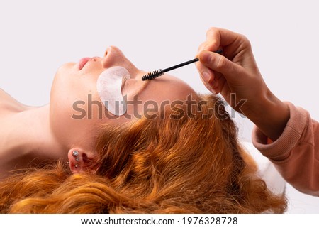 Eyebrow correction and eye makeup close-up. Master hands painting the shape of the eyebrows to a young ginger red-haired woman in a beauty salon. Business card template
