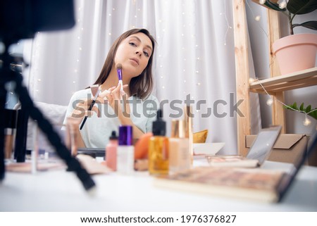 Happy woman vlogger is showing cosmetics products while recording video stream on phone. Concept Influencer blogger beauty blog.