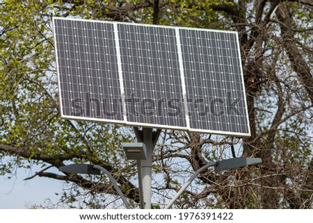 Solar panel on a pole in a city park. Close-up with blurred background.