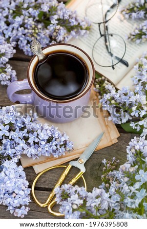 Spring time. The concept of good morning. A fancy purple coffee mug, an old book, glasses, and violet lilac. Top view.