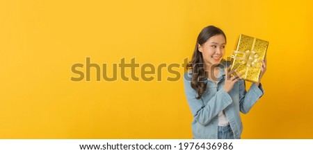 Happy birthday. wide banner. happy asian pretty woman in casual clothing jeans smiling and hold new year gift box over copy space yellow color background, christmas celebration, happy hew year concept