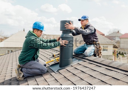 two Professional workmen's standing roof top and measuring chimney of new house under construction against blue background