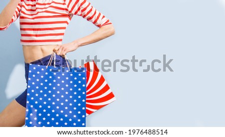 Happy shopping woman with shopping bags over blue background wearing striped clothing and shoping bags in patriotic colors