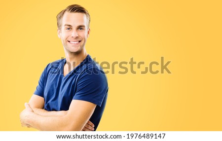 Portrait of young handsome happy man wearing in casual smart blue cloth, with crossed arms. Orange yellow color background, with copy space for text. Male model at studio concept picture. 