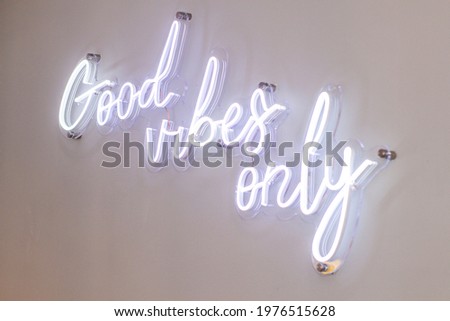Neon sign saying "only good vibes" in bright white color, on a white wall background,