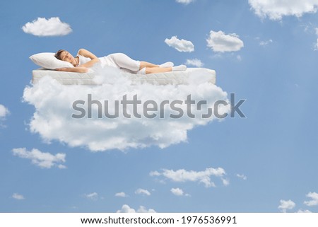 Young woman sleeping on a floating mattress up in the clouds and a blue sky Royalty-Free Stock Photo #1976536991
