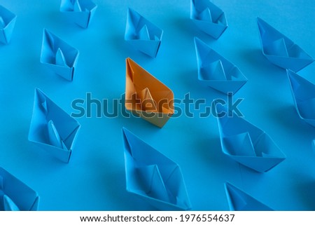 Origami in blue and orange on a blue paper background. An orange paper boat among many blue ones. Teamwork concept. Concept to stand out from the crowd.