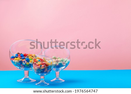 Glass containers with candies against pink background