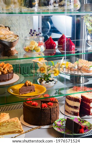 Various cakes with icing and desserts in refrigerated bakery case cabinet. Coconut shell dessert, chocolate cake and other sweets. Selective Focus