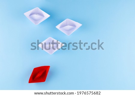 A group of white paper ship pointing in one direction and one red paper ship. Business behind an innovative solution concept.