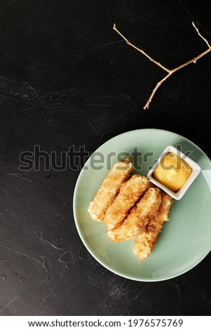 cheese sticks on a light plate on a black textured background with a golden sprig top view