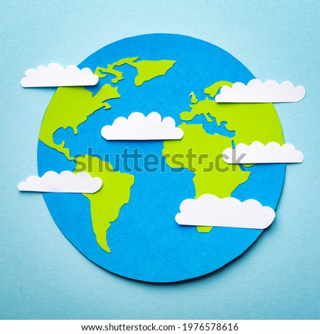 Paper cut concept of planet Earth on the blue background with paper clouds above.